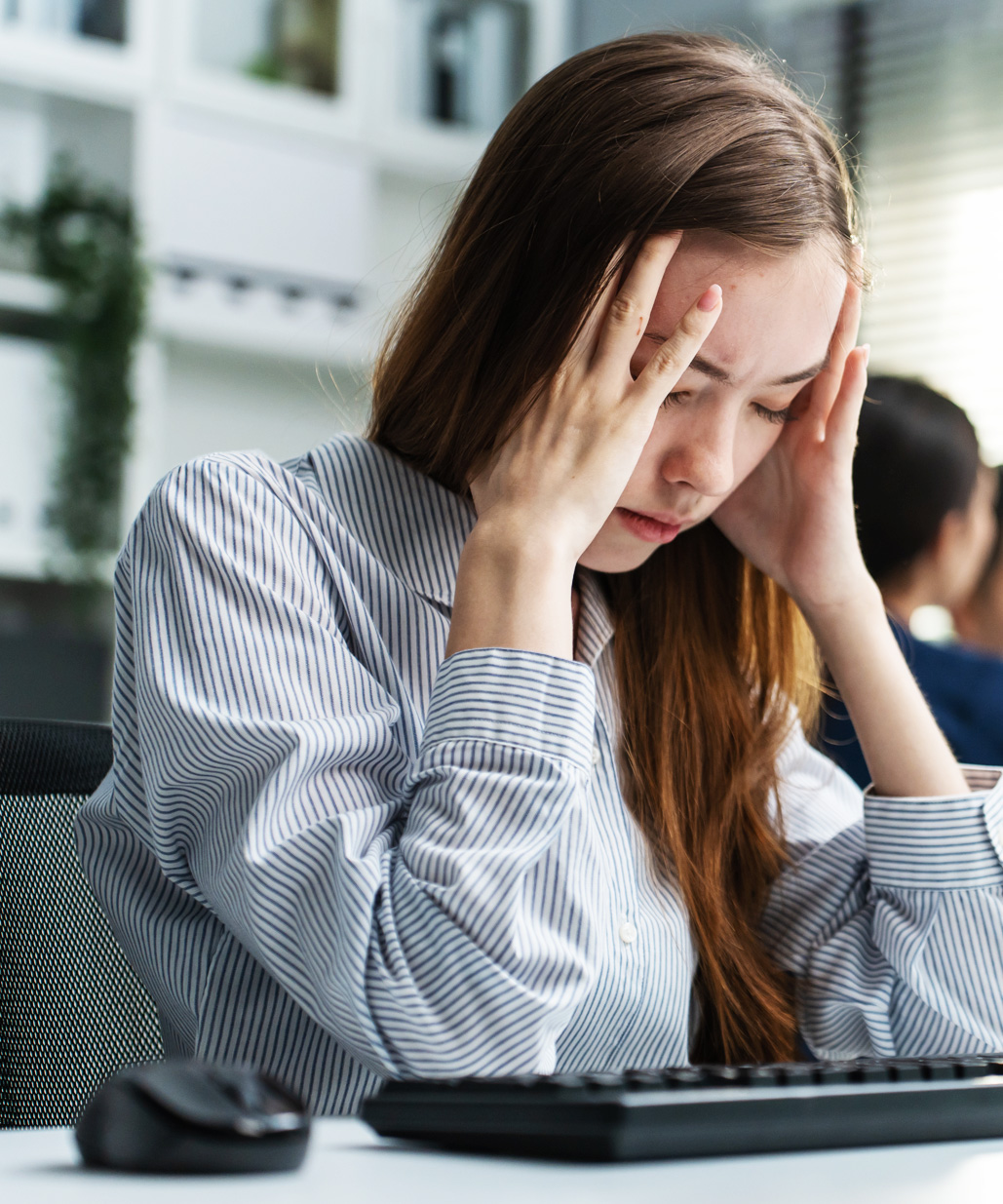 Gestresste Frau sitzt erschöpft am Schreibtisch, hält sich den Kopf und schließt die Augen – Symbolbild für Überforderung, Druck und den Verlust innerer Balance im Berufsalltag.